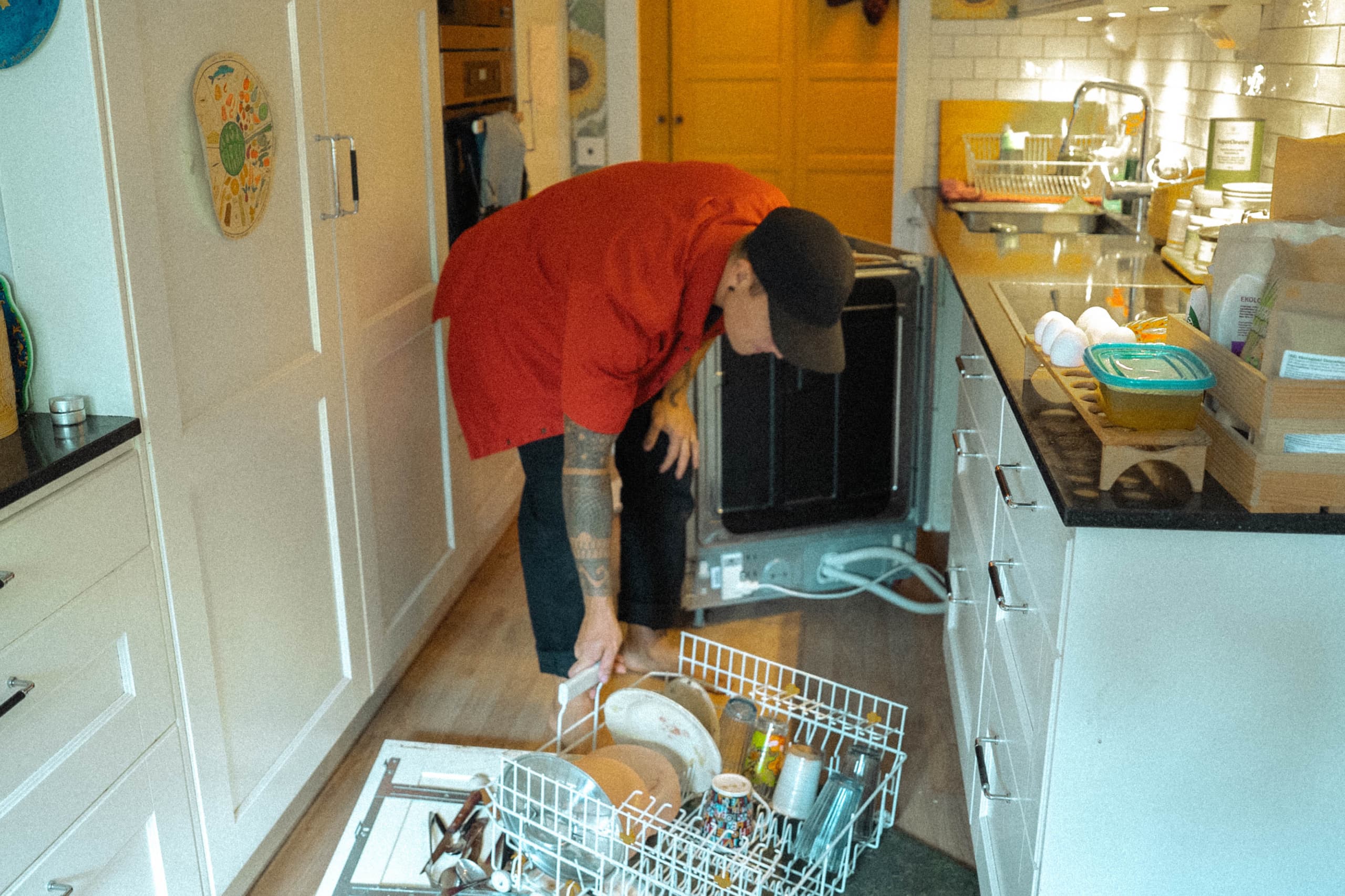 Person i röd tröja som plockar ur diskmaskinen i ett kök