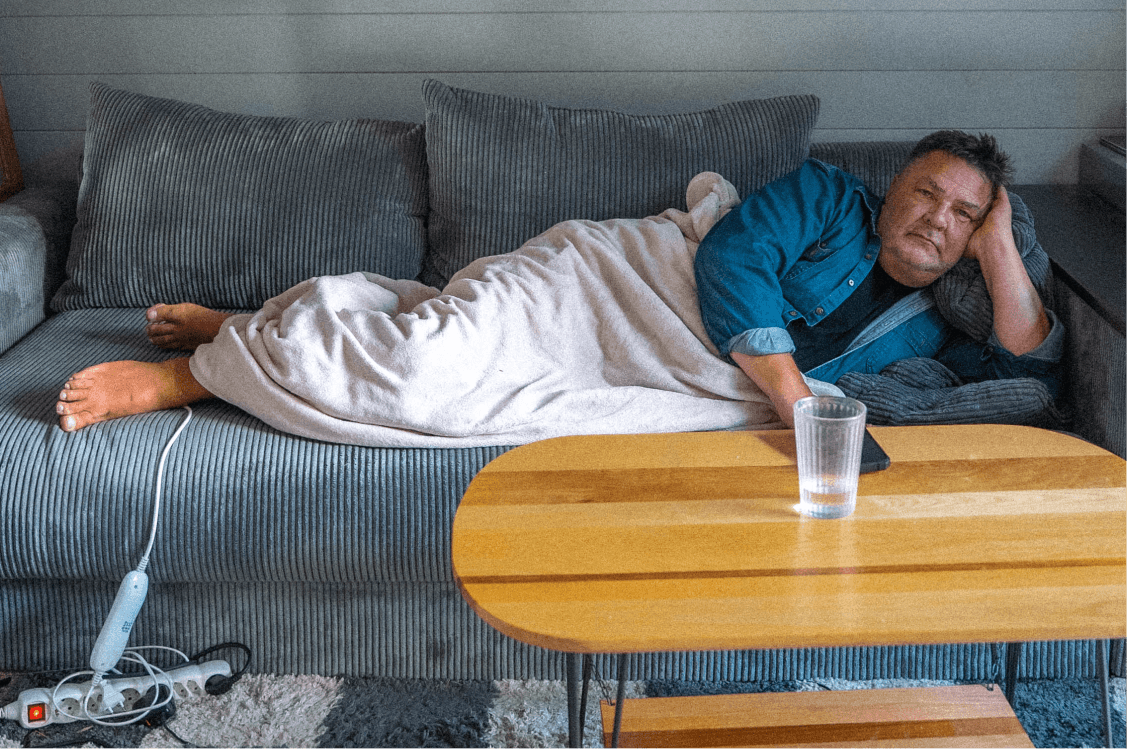 Man som vilar på en soffa med en filt över benen