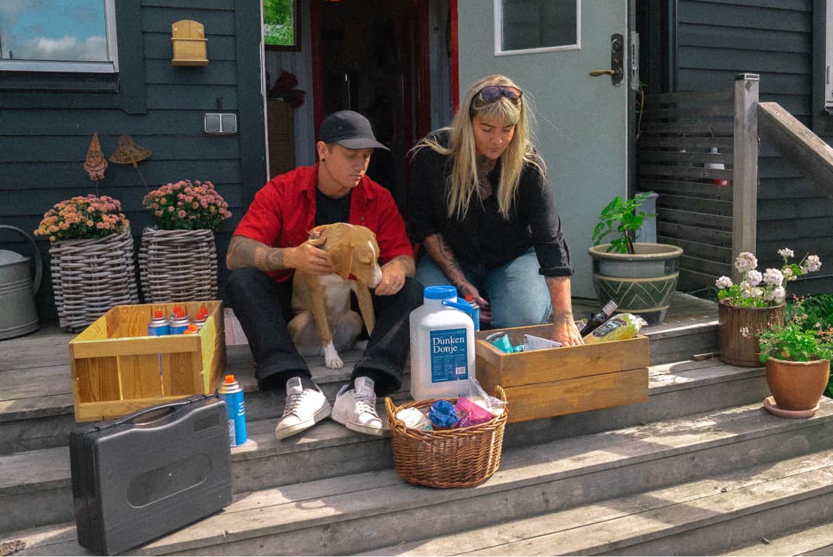 Vicky and Timothy on their porch steps with the dog, surrounded by toolboxes and crates