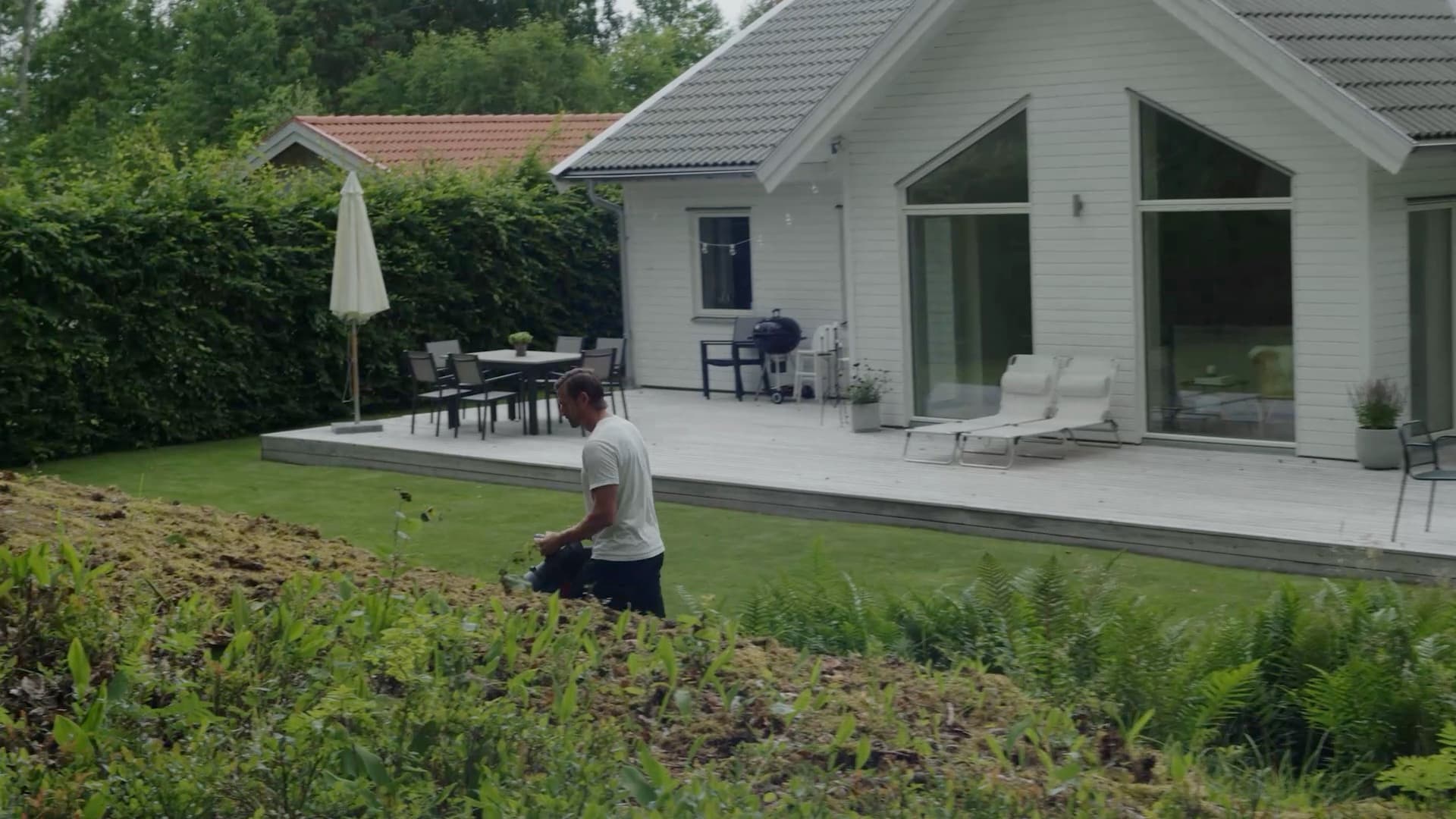 Man with a leaf blower on the lawn beside a white house with a deck